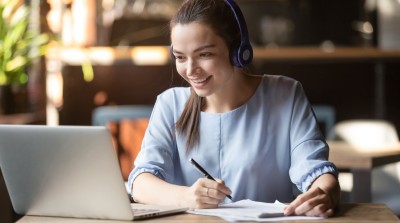 eine lächelnde Frau arbeitet mit Headset am Laptop