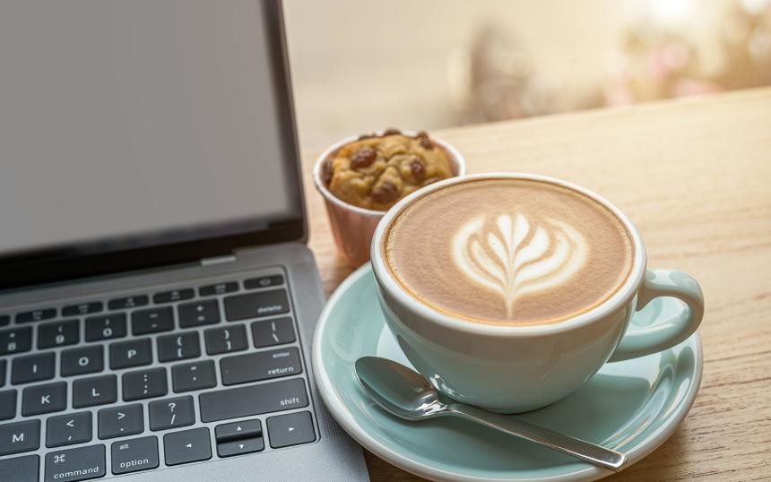 Kaffeetasse steht neben einem Laptop, auf dem Hände tippen