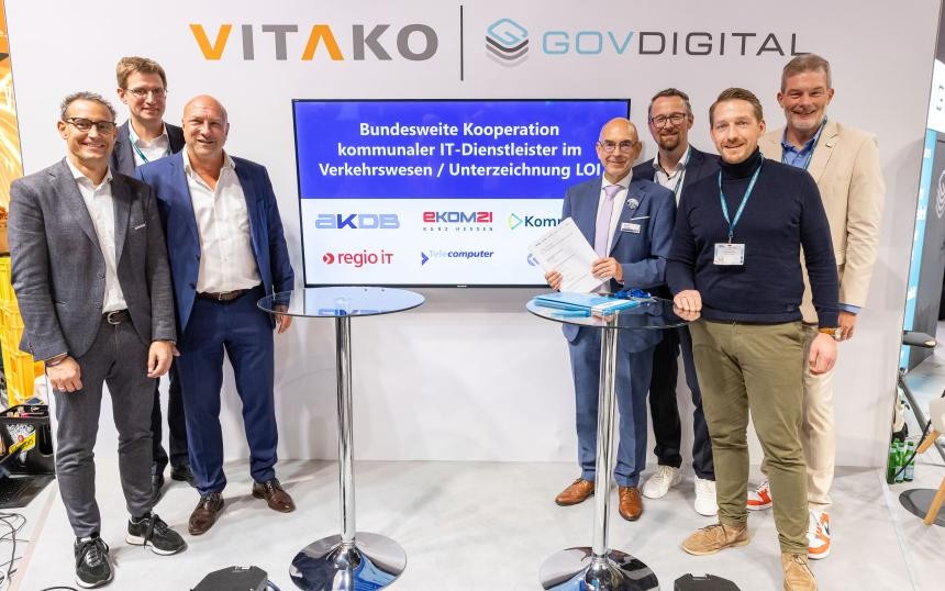 Sieben Männer, die an zwei Stehtischen stehen und einen Vertrag unterzeichnen